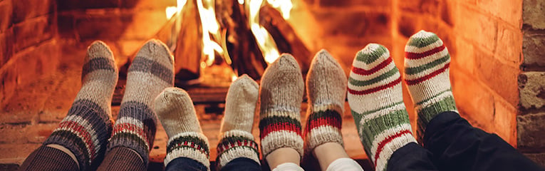 Family mother, father and kids wearing warm woolen socks warming feet by fireplace on Christmas time