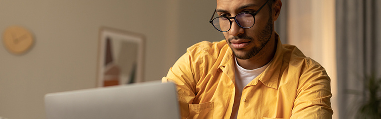 Focused millennial black man in glasses using laptop, working online, having online business meeting at home office