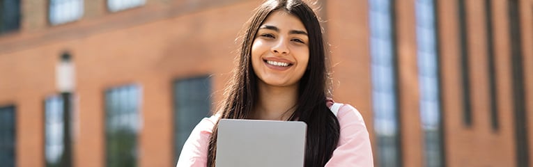 Portrait of happy hispanic lady student posing with laptop in hands outdoors, looking and smiling at camera