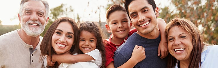 Three generation Hispanic family standing in the park, smiling to camera,