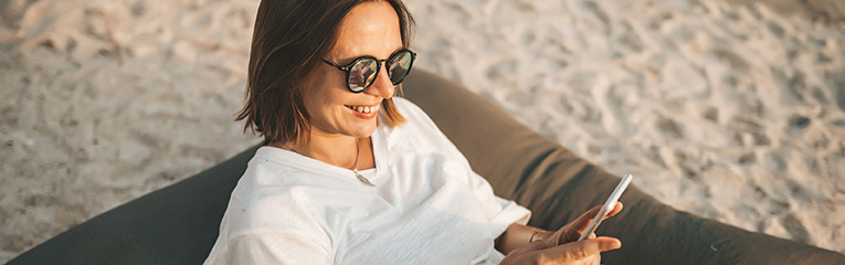 Woman in sunglasses using phone relaxing on beanbag at the beach