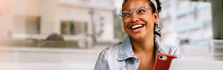 Happy female student sitting in a coffee shop, using a smartphone