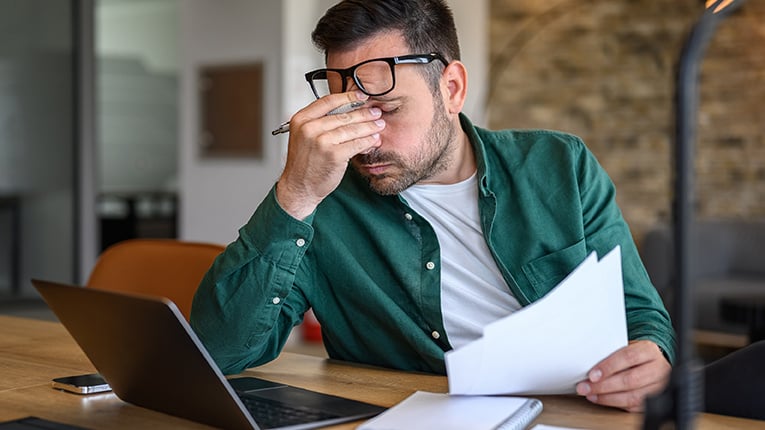 Anxious male financial advisor rubbing eyes while working over laptop and analyzing reports at desk