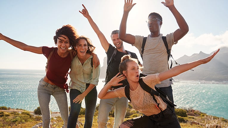 Millennial friends on a hiking trip celebrate reaching the summit and have fun posing for photos