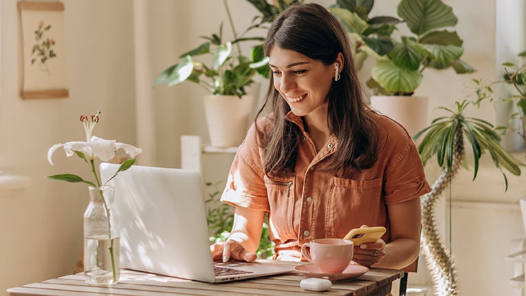 Positive young mixed race woman using a laptop and smartphone at home