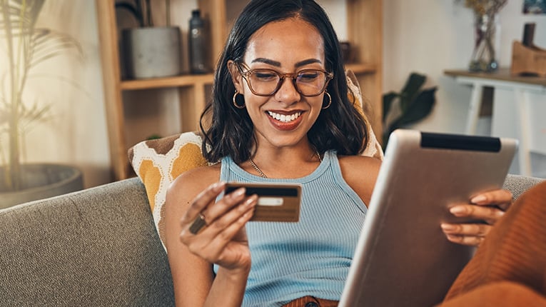 Smiling mixed race woman using credit card for ecommerce on digital tablet at home