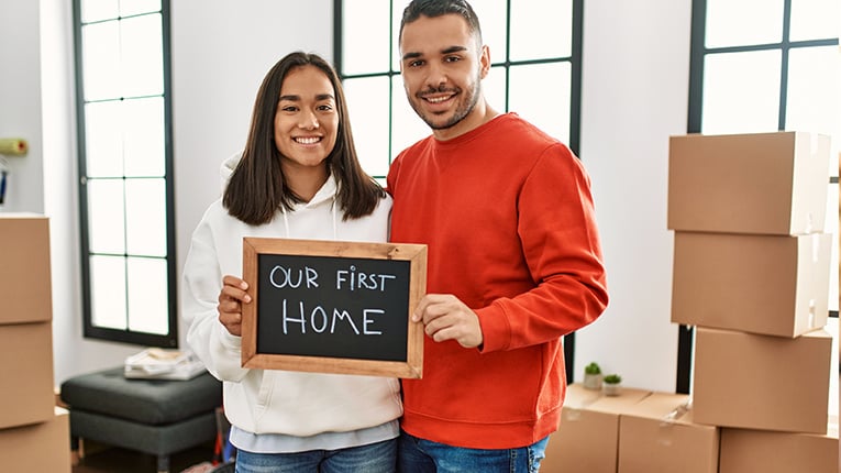 Young latin couple smiling happy holding blackboard with our first home message