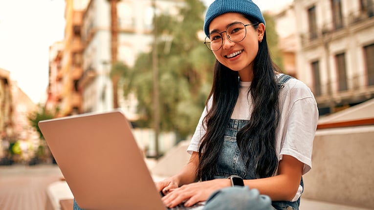 Young Asian woman smiling with laptop on her lap. 