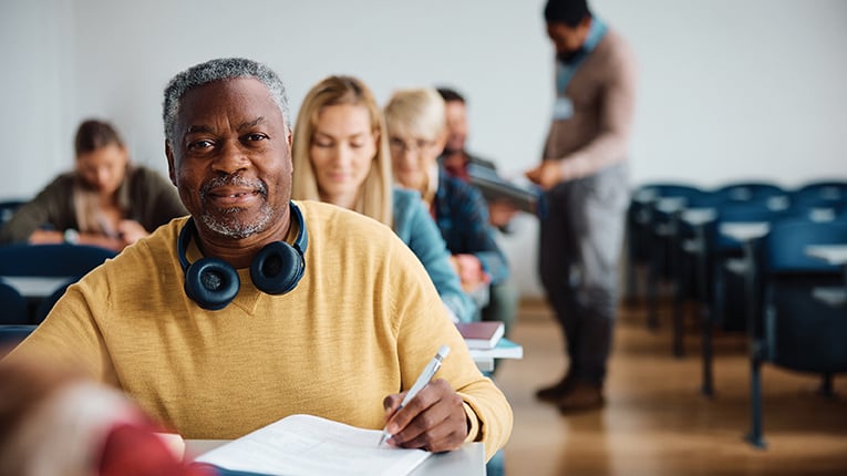 African American man with yellow shirt and headphones around his neck sitting in classroom